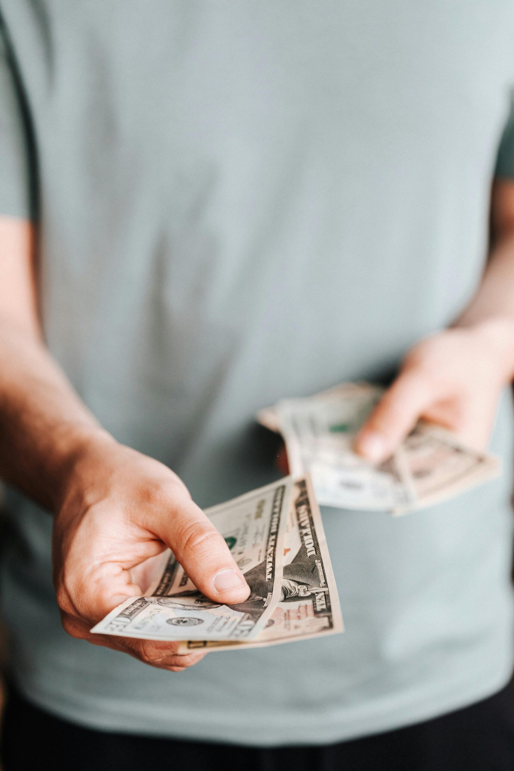 Close-up of an unrecognizable man holding dollar bills with a blurred background indoors.